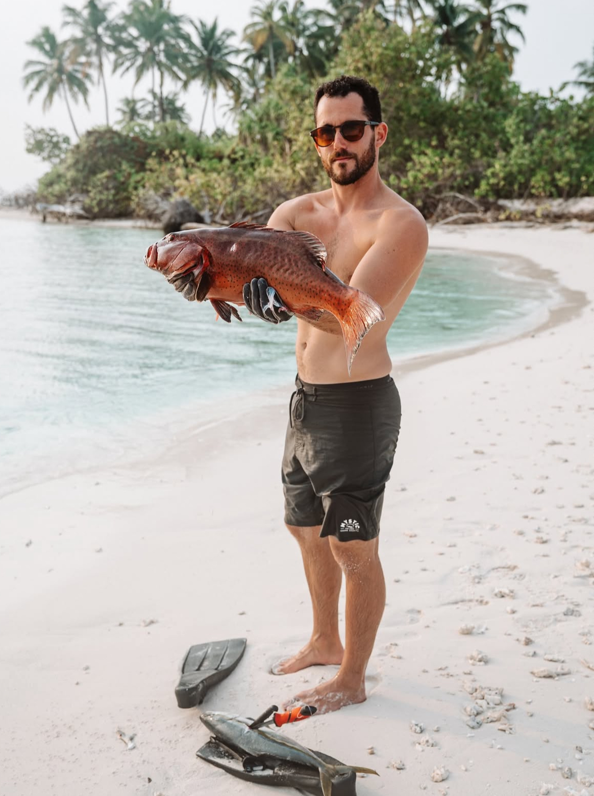 Guest holding a coral trout on a white sand beach in the Maldives