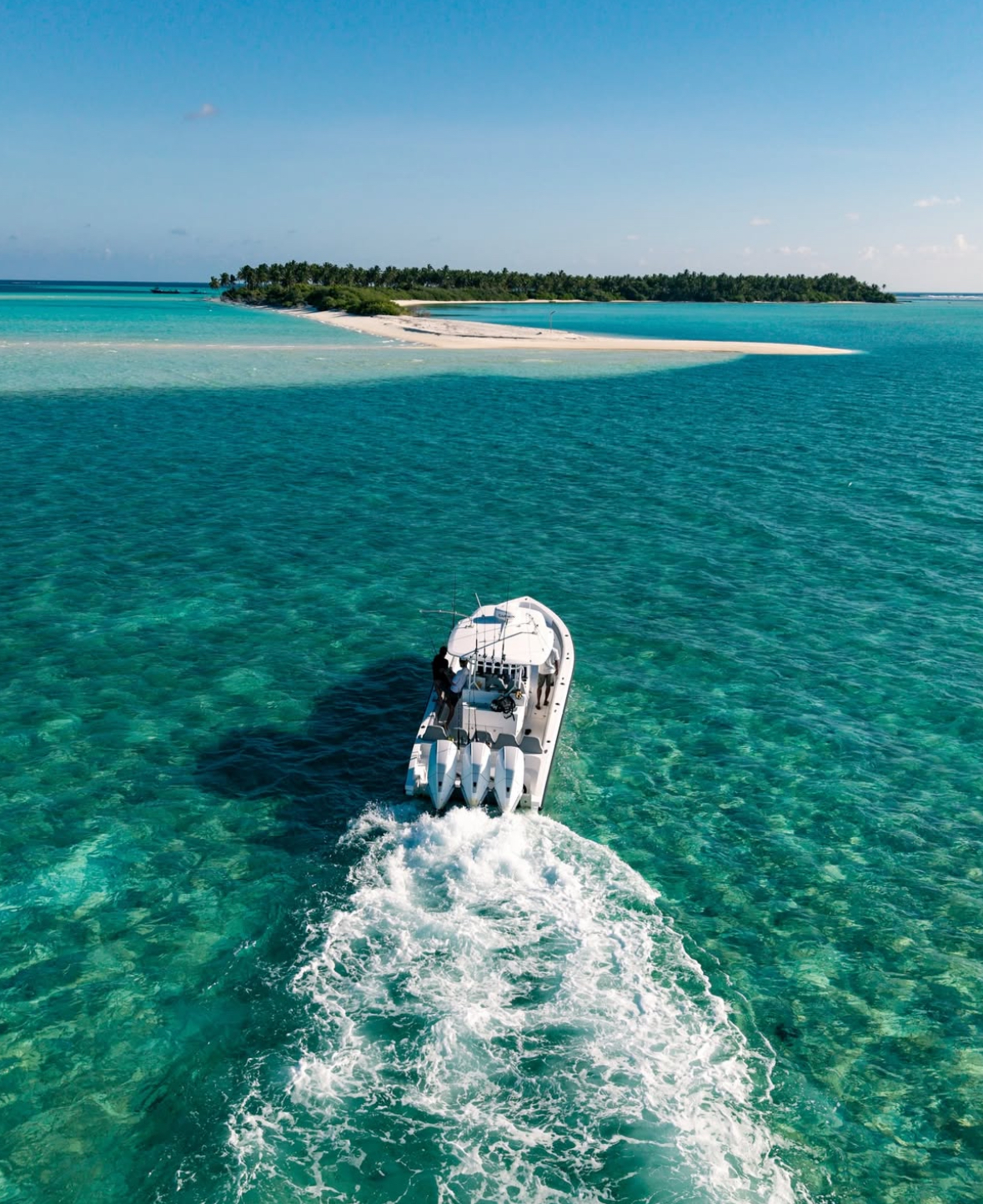 Drone shot of fishing boat cruising turquoise waters near an island in South Ari Atoll